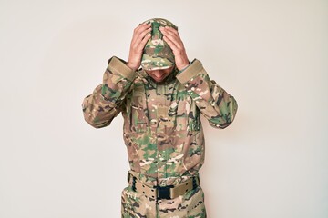 Young caucasian man wearing camouflage army uniform suffering from headache desperate and stressed because pain and migraine. hands on head.