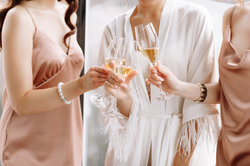 Morning of bride. Gorgeous bride with best bridesmaids are holding glasses and drinking champagne in hotelroom near the large window. Sexy bridesmaids in exciting negligee. Wedding morning details