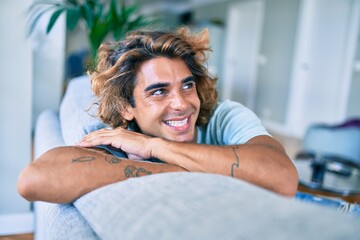 Young hispanic man smiling happy sitting on the sofa at home