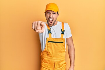 Young handsome man wearing handyman uniform over yellow background pointing displeased and frustrated to the camera, angry and furious with you