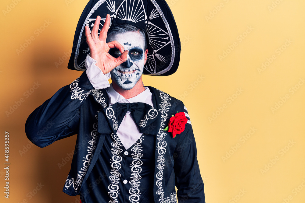 Poster young man wearing mexican day of the dead costume over yellow smiling happy doing ok sign with hand 