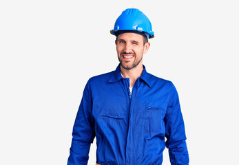 Young handsome man wearing worker uniform and hardhat winking looking at the camera with sexy expression, cheerful and happy face.