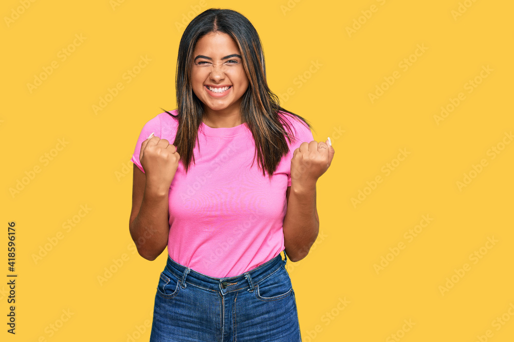 Wall mural Young latin girl wearing casual clothes excited for success with arms raised and eyes closed celebrating victory smiling. winner concept.