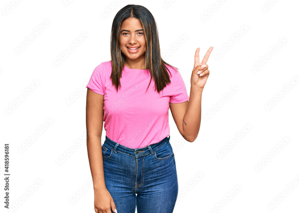 Poster Young latin girl wearing casual clothes smiling with happy face winking at the camera doing victory sign. number two.