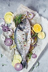 Fresh fish dorado. Raw dorado with herbs, spices and lemon and lime slices ready to cook on a gray background. Top view.  Fresh fish gilt-head bream  with salt, herbs and pepper.