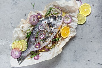 Fresh fish dorado. Raw dorado with herbs, spices and lemon and lime slices ready to cook on a gray...