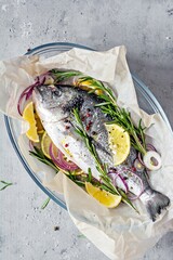 Fresh fish dorado. Raw dorado with herbs, spices and lemon and lime slices ready to cook on a gray background. Top view.  Fresh fish gilt-head bream  with salt, herbs and pepper.