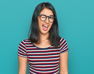 Beautiful asian young woman wearing casual clothes and glasses winking looking at the camera with sexy expression, cheerful and happy face.