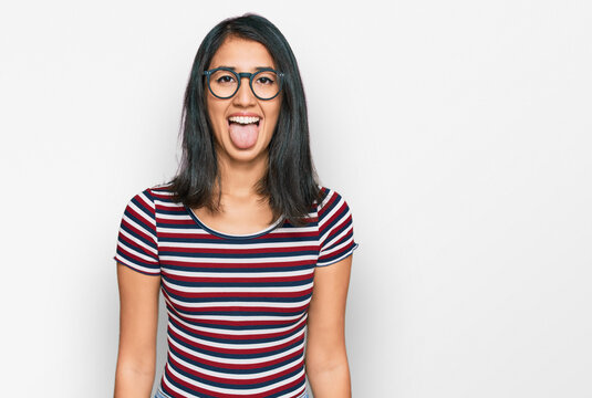 Beautiful asian young woman wearing casual clothes and glasses sticking tongue out happy with funny expression. emotion concept.