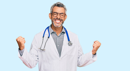 Middle age grey-haired man wearing doctor uniform and stethoscope very happy and excited doing winner gesture with arms raised, smiling and screaming for success. celebration concept.