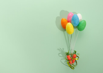 Yellow, white, pink, green, orange and blue egg on the wire look like balloons. two carrots ride with them. Flat lay on green background.