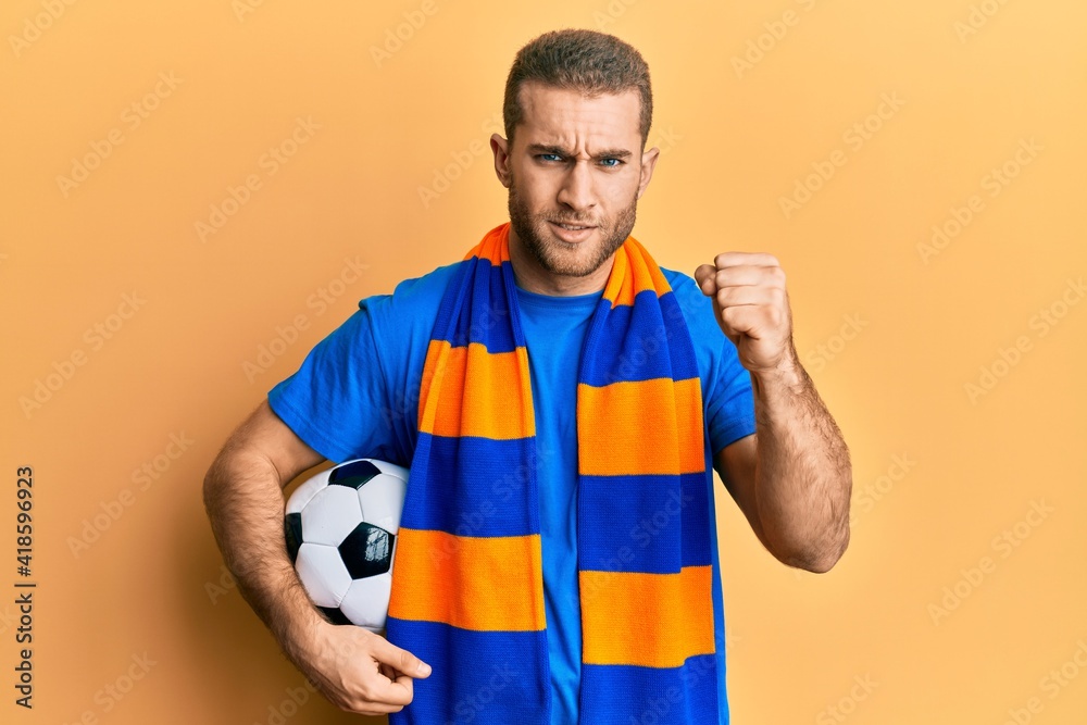 Canvas Prints Young caucasian man football hooligan cheering game holding ball annoyed and frustrated shouting with anger, yelling crazy with anger and hand raised