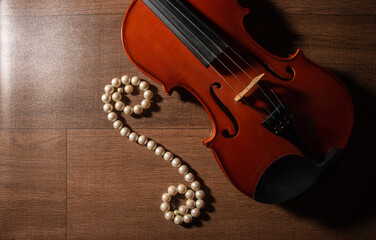 Fototapeta na wymiar Violin and pearl necklace, arrangement with violin and pearl necklace on wooden surface, low key portrait, top view.
