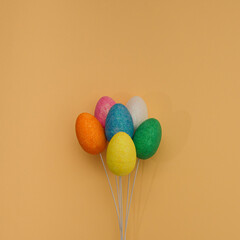 Yellow, white, pink, green, orange and blue egg on the wire look like balloons. Flat lay on orange background.