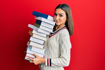 Young brunette student girl holding a pile of books skeptic and nervous, frowning upset because of problem. negative person.