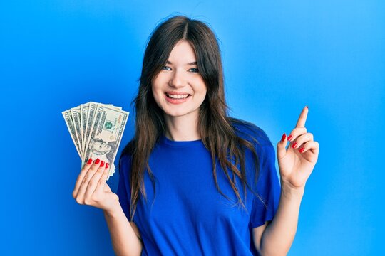 Young beautiful caucasian girl holding 20 dollars banknote smiling happy pointing with hand and finger to the side