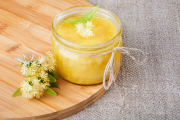 Glass honey jar with linden flowers on a  wooden board. Copy space