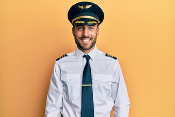 Handsome hispanic man wearing airplane pilot uniform with a happy and cool smile on face. lucky...
