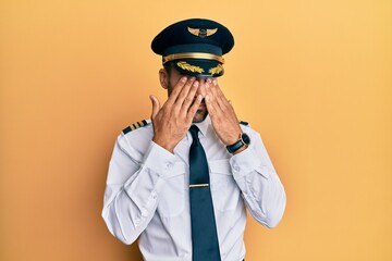 Handsome hispanic man wearing airplane pilot uniform rubbing eyes for fatigue and headache, sleepy...
