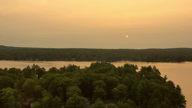 Aerial shot of houses amidst trees at lakeshore, drone descending backward over lake against sky at sunset - Berkshire County, Massachusetts