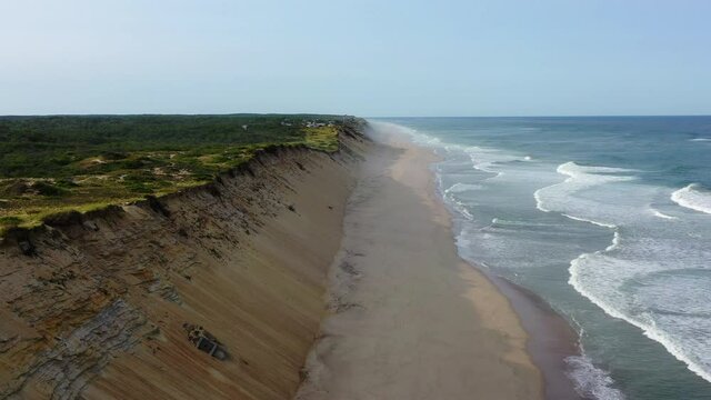 Aerial shot of waves splashing on shore at beach against sky, drone flying backward over coastline on sunny day - Cape Cod, Massachusetts