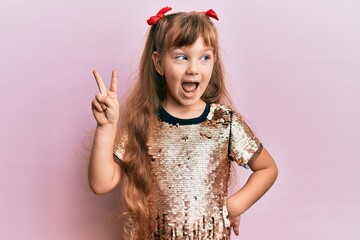 Little caucasian girl kid wearing festive sequins dress showing and pointing up with fingers number two while smiling confident and happy.
