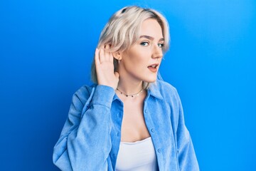 Young blonde girl wearing casual clothes smiling with hand over ear listening and hearing to rumor...