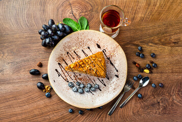 a piece of honey cake on a plate, decorated with chocolate and blueberries
