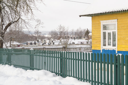 An old cemetery with tombstones and large wooden crosses in belarussian village with old wooden rustic houses. Western Belarus.