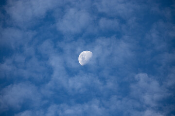 White cotton-textured clouds spread across a blue sky whit moon 