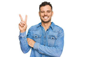 Young hispanic man wearing casual denim jacket smiling with happy face winking at the camera doing...