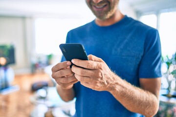 Young irish man smiling happy using smartphone standing at home.
