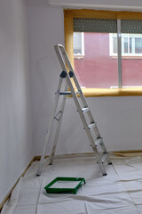 Painter's staircase in a room just painted white, next to a window.