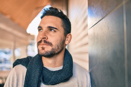 Young hispanic man smiling happy wearing scarf leaning on the wall at the city.
