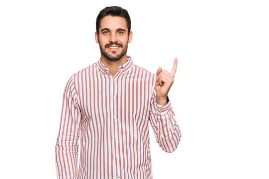 Young hispanic man wearing business shirt with a big smile on face, pointing with hand and finger to the side looking at the camera.