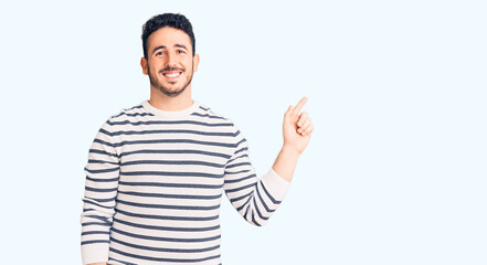 Fototapeta premium Young hispanic man wearing casual clothes with a big smile on face, pointing with hand finger to the side looking at the camera.