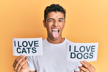 Young handsome african american man holding paper with i love cats and i love dogs phrase sticking tongue out happy with funny expression.