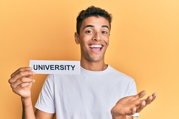 Young handsome african american man holding paper with university word celebrating achievement with happy smile and winner expression with raised hand