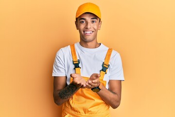 Young handsome african american man wearing handyman uniform over yellow background smiling with hands palms together receiving or giving gesture. hold and protection