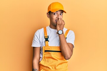 Young handsome african american man wearing handyman uniform over yellow background looking stressed and nervous with hands on mouth biting nails. anxiety problem.
