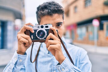 Young latin tourist man smiling happy using vintage camera walking at the city.