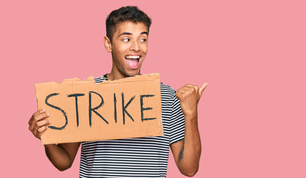 Young handsome african american man holding strike banner cardboard pointing thumb up to the side smiling happy with open mouth
