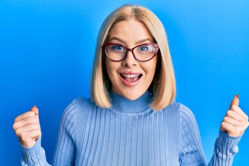 Young blonde woman wearing casual clothes and glasses celebrating surprised and amazed for success with arms raised and open eyes. winner concept.