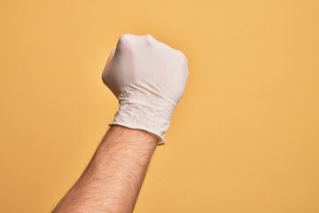 Hand of caucasian young man with medical glove over isolated yellow background doing protest and...