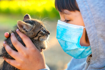 Little girl with mask playing with her cat during the coronavirus pandemic