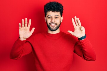 Young arab man with beard wearing casual red sweater showing and pointing up with fingers number nine while smiling confident and happy.