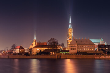 Obraz premium Cathedral of St. John the Baptist, Collegiate Church of the Holy Cross and Saint Bartholomew in Wroclaw on the Odra River, illuminated at night.
