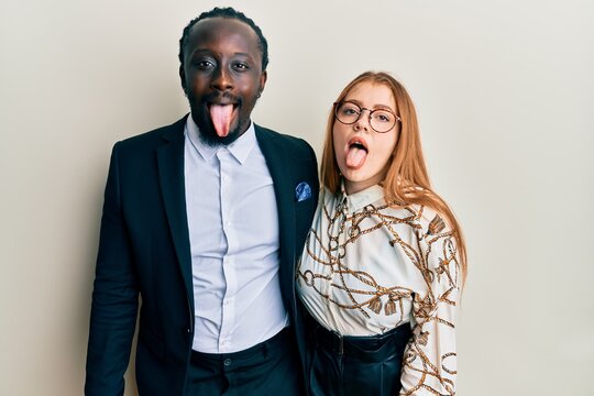 Young interracial couple wearing business and elegant clothes sticking tongue out happy with funny expression. emotion concept.