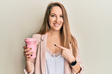 Young blonde woman drinking a take away cup of coffee smiling happy pointing with hand and finger