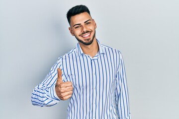 Fototapeta premium Young hispanic man with beard wearing casual striped shirt doing happy thumbs up gesture with hand. approving expression looking at the camera showing success.